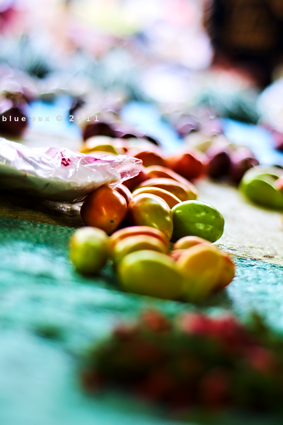 A close-up of small multicolored tomatoes spread across a teal cloth at a market stall, with shallow depth of field blurring the background into soft bokeh.
