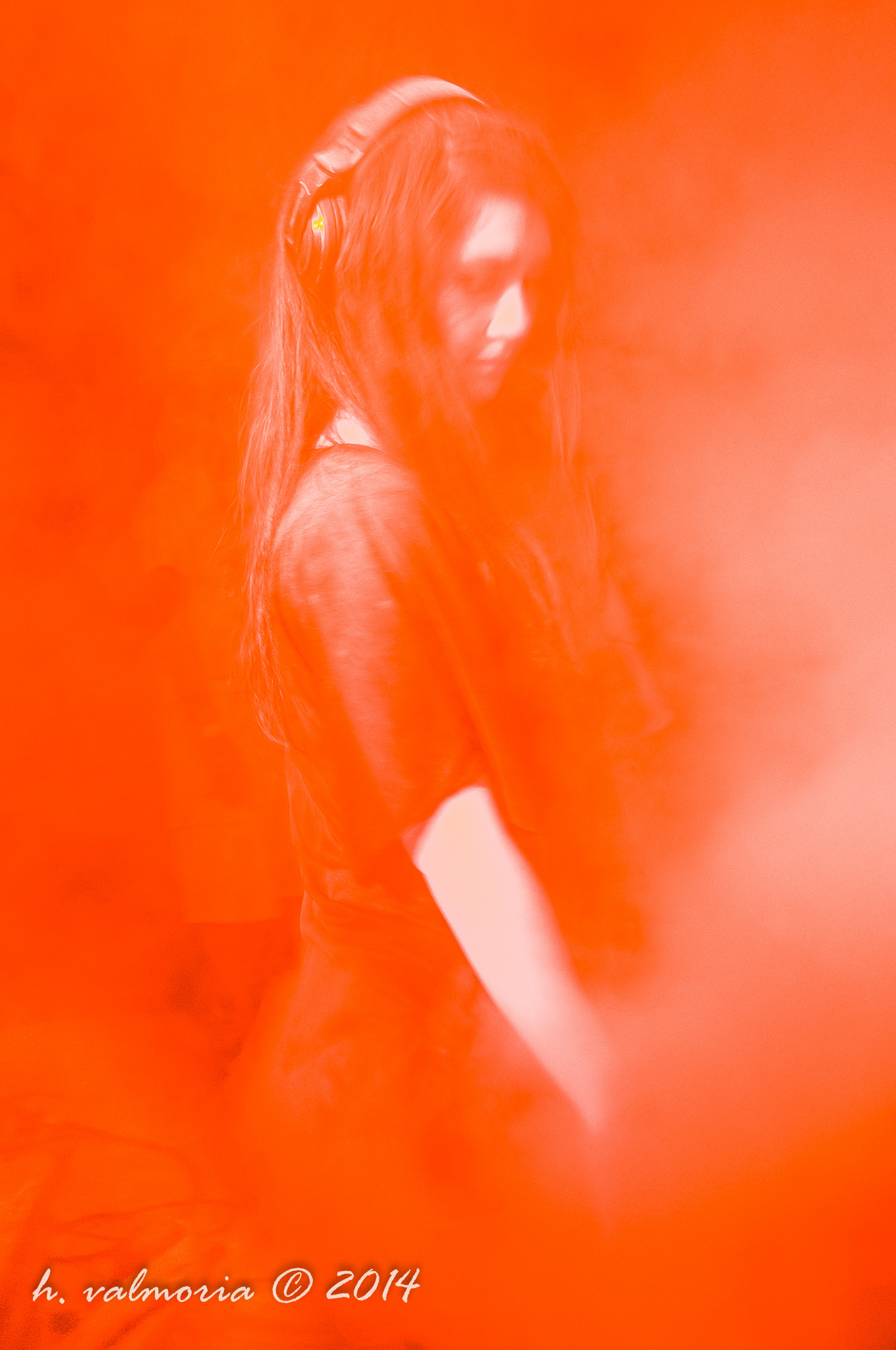 A young woman wearing headphones stands in profile against an overwhelming red-orange background, her long hair loose and her gaze cast downward in quiet introspection, the image bathed entirely in a monochromatic red wash.